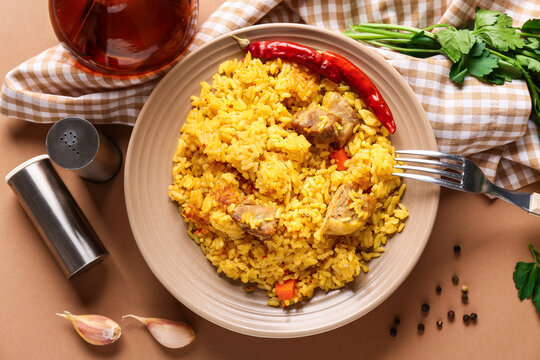 Plate of tasty pilaf with chili pepper, garlic and parsley on brown background