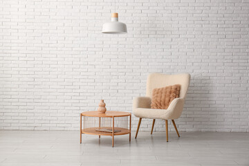 Stylish armchair with wooden table and hanging lamp near white brick wall in living room