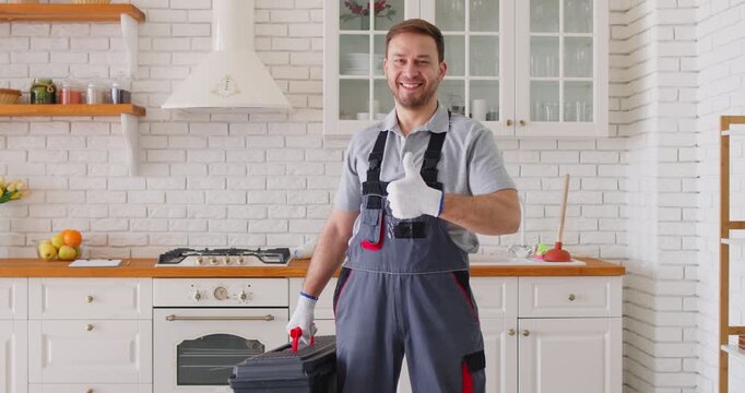 Portrait of a happy and smiling man working as a plumber, giving a thumbs-up in the kitchen at home. The professional holds a tool, symbolizing service, repair work, and plumbing expertise.