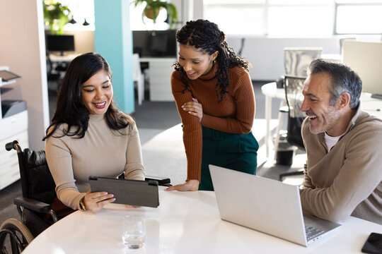 Diverse coworkers collaborating on tablet and laptop at conference table with wheelchair