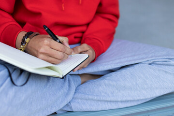 Open lined notebook lying on grey floor while black pen scribbling notes near beaded bracelets