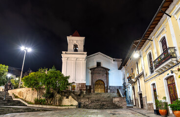 San Blas Church stands near the historic center of Quito, Ecuador. Colonial white Catholic church features stone entrance and bell tower illuminated under night sky