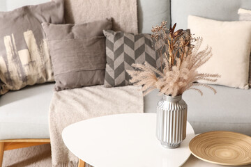 Vase with beautiful flowers on table near stylish grey sofa in living room