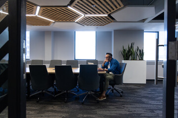 Professional sitting at office conference table with chairs, working on laptop near window