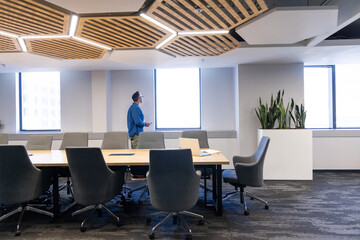 Table and swivel chairs are arranged under hexagonal LED ceiling panels by planter and windows