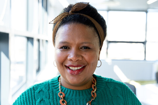 Mid adult African American woman wearing teal sweater and chunky necklace smiling by grid windows