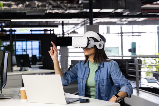 VR headset resting on desk near windows revealing greenery in office, with laptop and coffee cup