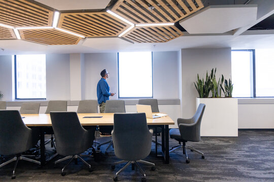 Table and swivel chairs are arranged under hexagonal LED ceiling panels by planter and windows
