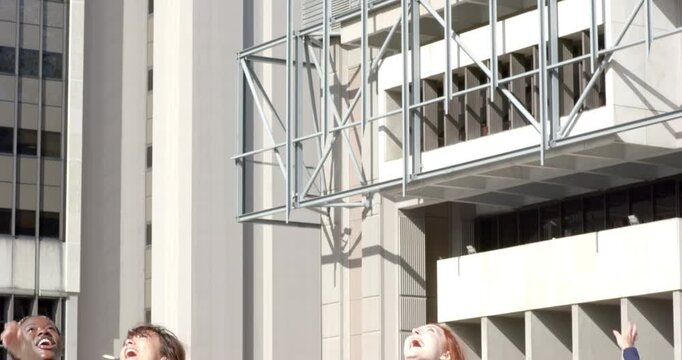 Female graduates celebrating graduation by tossing caps and holding diplomas on plaza by columns - Powered by Adobe