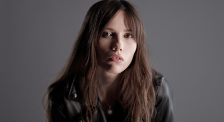 Studio portrait of a beautiful brunette woman with long hair wearing a leather jacket on a gray background. This image is suitable for fashion beauty and lifestyle projects.