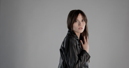Studio portrait of a brunette woman wearing a black leather jacket against a grey background. This image is suitable for fashion and beauty projects as well as editorial.