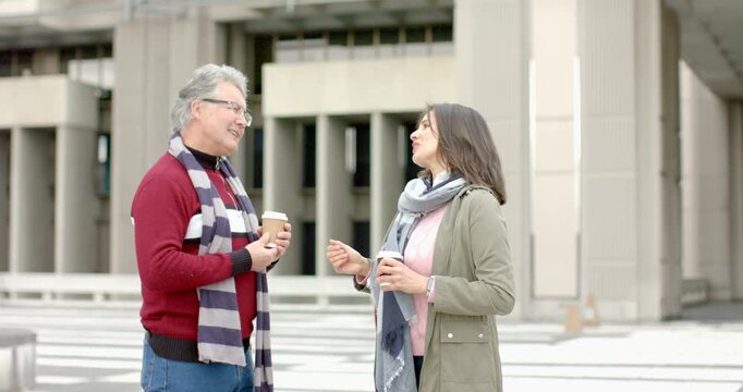 Diverse coworkers meeting formally on office plaza, talking, shaking hands and swapping coffee cups