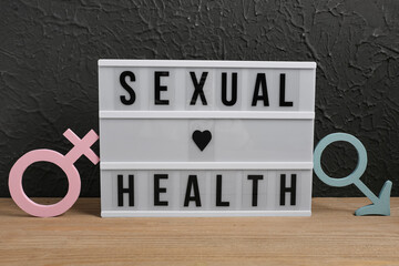 Board with text SEXUAL EDUCATION, male and female symbols on table against dark grunge background