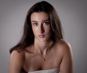 Naklejka premium Studio portrait of a beautiful brunette woman with natural makeup and bare shoulders against a gray background. This image is suitable for fashion beauty and advertising projects.