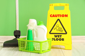 Trolley with cleaning supplies and caution sign near green wall