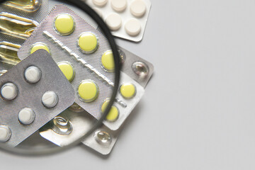 Magnifier with different pills on grey background