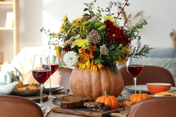 Pumpkin with autumn bouquet on festive dining table in room, closeup