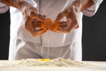 Young chef preparing dough for bread on table against black background