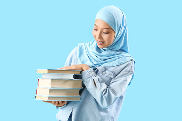 Beautiful young Asian woman in hijab with books on blue background