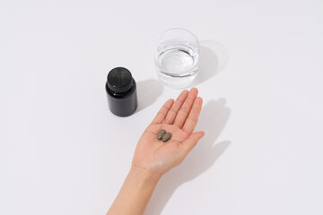 Hand holding pills with water and supplement bottle on white background