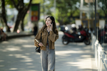 Obraz premium Asian woman talking on phone walking urban street
