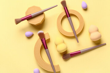 Decorative podiums with makeup brushes and sponges on yellow background