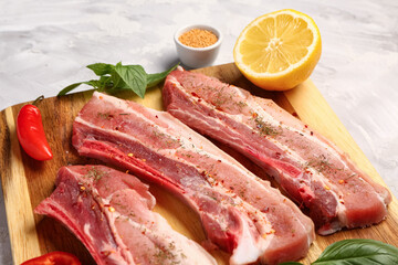 Wooden board with raw pork ribs, lemon and spices on grunge background, closeup