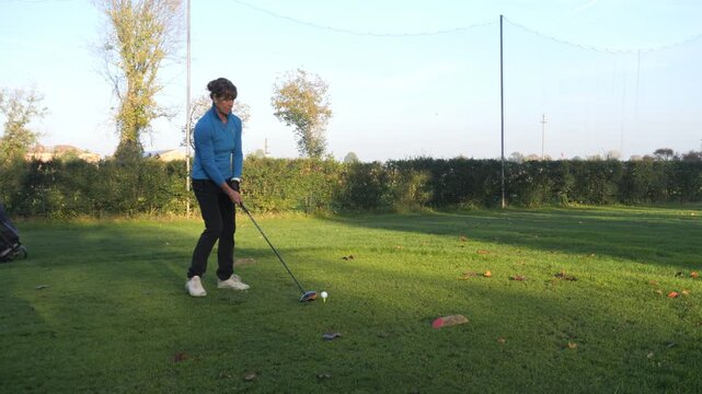 Middle-aged woman executing a powerful tee shot on a sunny golf course, focused and athletic during outdoor practice, enjoying leisure, sport and healthy active lifestyle