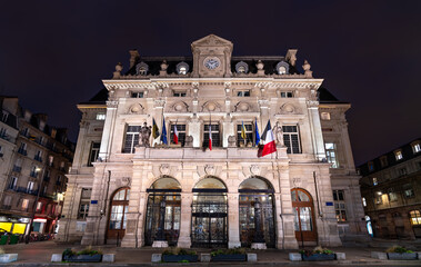 Town Hall of the 18th arrondissement in Paris, France. The historic building with a clock tower and flags stands on Place Jules Joffrin at night