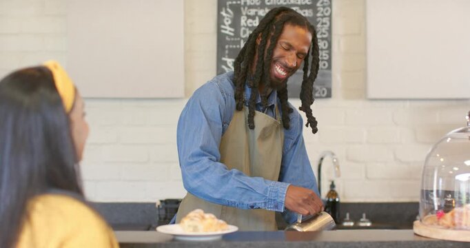After order placement, African American barista pouring steamed milk from pitcher at coffee counter