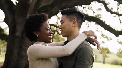 Diverse couple embracing in nature, near a large tree, bathed in soft light, sharing a warm, intimate moment