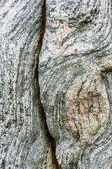 Closeup of weathered rock of a standing stone with large crack, lines and patterns in gray and orange, and bits of lichen, as a nature background
