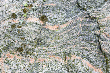 Obraz premium Closeup of weathered rock of a standing stone with wavy curved lines if gray and orange, and bits of lichen, as a nature background 