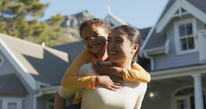 Entering view diverse mother and daughter piggybacking, walking on lawn and celebrating sunny day