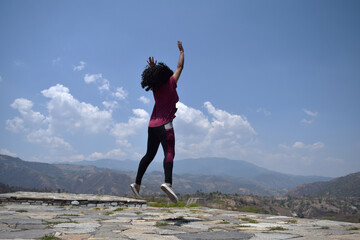 Photograph of a woman with short, praying hair jumping in some outdoor ruins with a clear sky