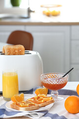 Plate with delicious orange jam toasts, glass of juice and modern toaster on table in kitchen
