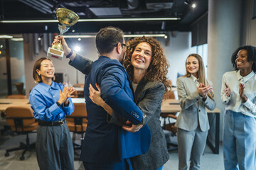 Business colleagues hugging celebrating success with trophy in office