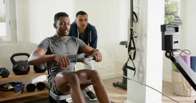 African American client initiating stroke on rowing machine at home gym with trainer coaching form