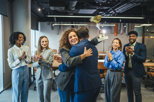 Businesswoman receiving award, embracing colleague while team applauding