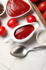Gravy boat and bowl of tasty ketchup with fresh tomatoes on white tile background