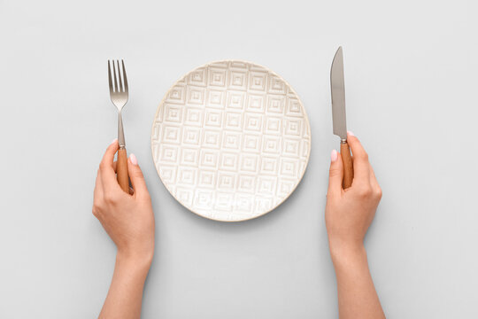 Woman with cutlery and empty plate on grey background