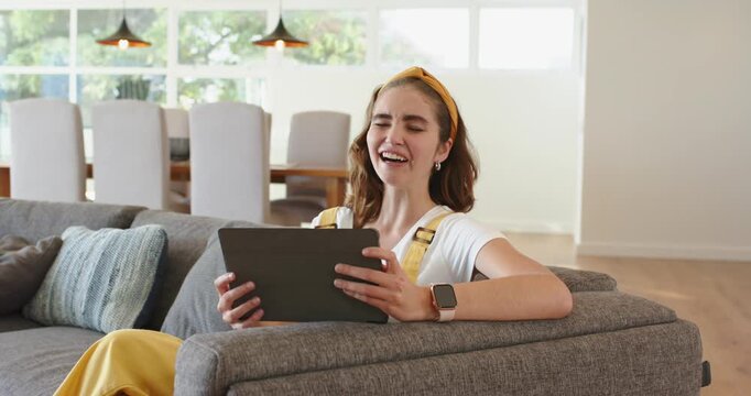 Woman in shirt sitting on sofa at home scrolling tablet grimacing at content before smiling again
