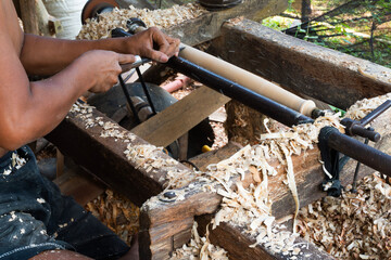 Artisan's hands operating a traditional wood lathe surrounded by wood shavings.