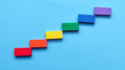 Rainbow Colored Wooden Blocks Arranged as Ascending Steps or Staircase on a Bright Blue Background for Progress Concept