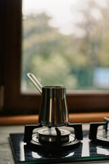Stove with a metal kettle resting on a lit burner in a cozy kitchen, natural light from a window, capturing a calm, domestic cooking moment.