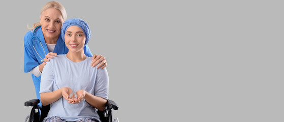 Young woman after chemotherapy in wheelchair with grey awareness ribbon and nurse on light...
