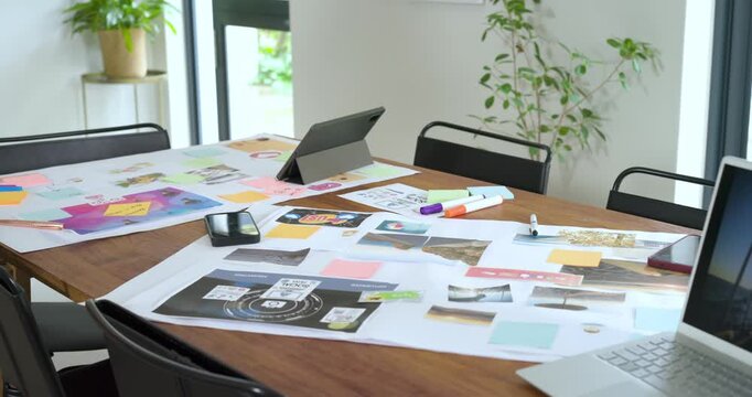 Camera is panning across wooden tabletop and scattered design tools to reveal full office workspace