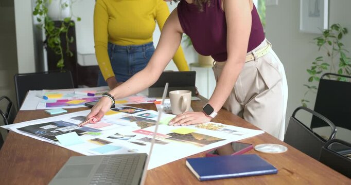 Using photos and notes, diverse female coworkers are arranging board at table and finalizing design