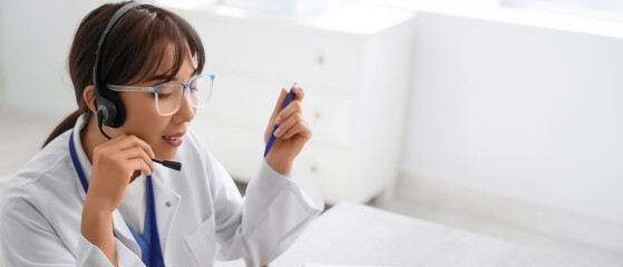Female Asian doctor with headset giving online consultation in clinic, closeup