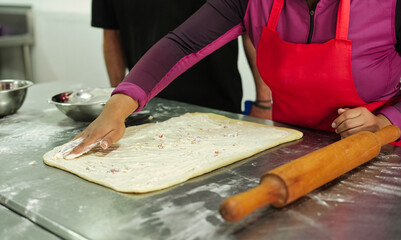 Woman spreading cream on dough with hand in kitchen